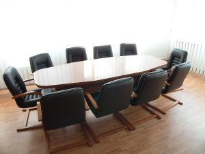 An oval-shaped wood conference table surrounded by black office chairs